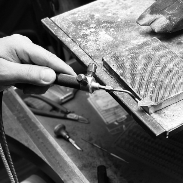Person using pliers to manipulate a small metal object on a workbench with tools around.