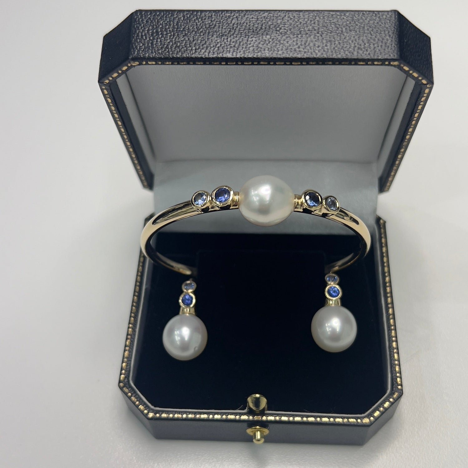 Pearl bracelet and earrings set in a black jewelry box on a light gray background